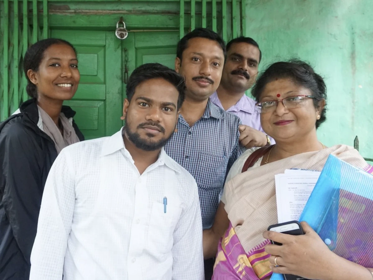Student standing with local community members in front of a green-painted building during a field practicum in India.
